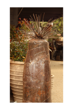 A rustic metal sculpture of a grass tree on a decorative background