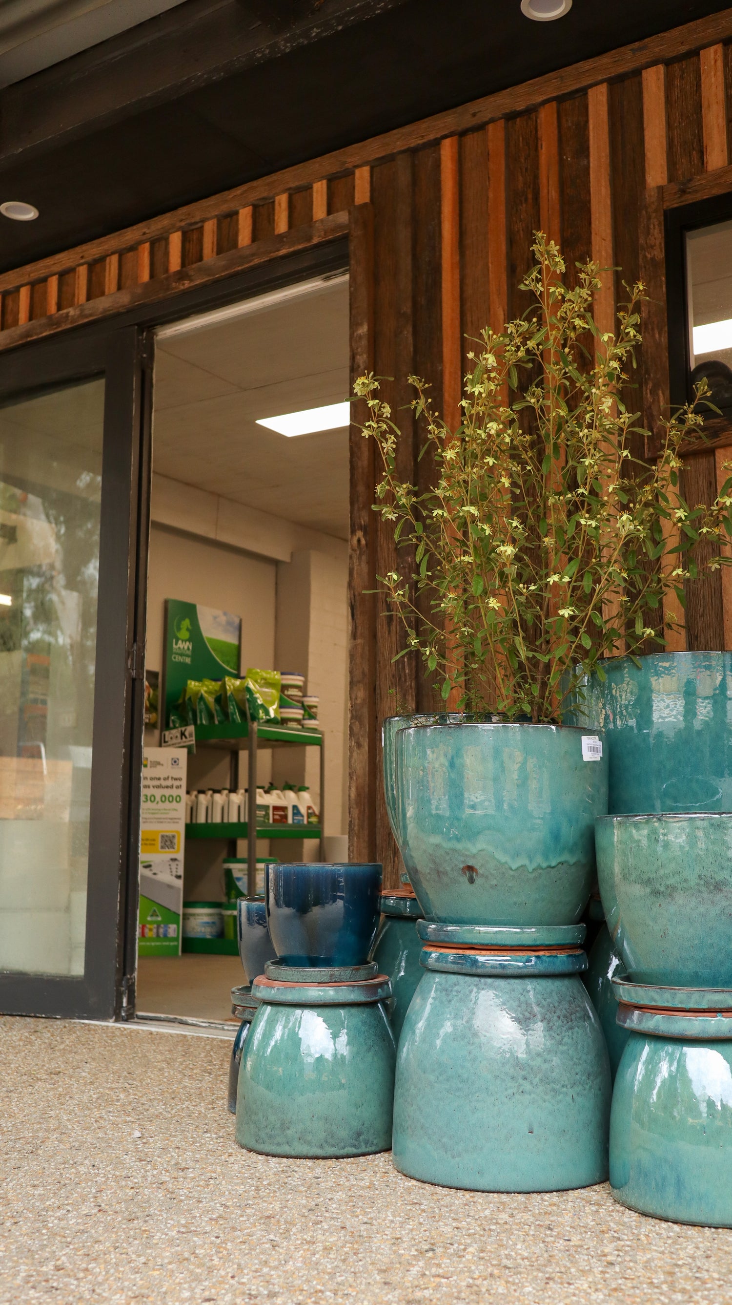 Stack of teal ceramic pots with plants inside, in front of a store entrance.