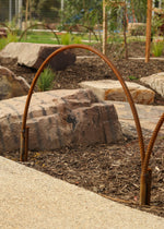 Rustic metal hoop in a garden setting with rocks and plants.