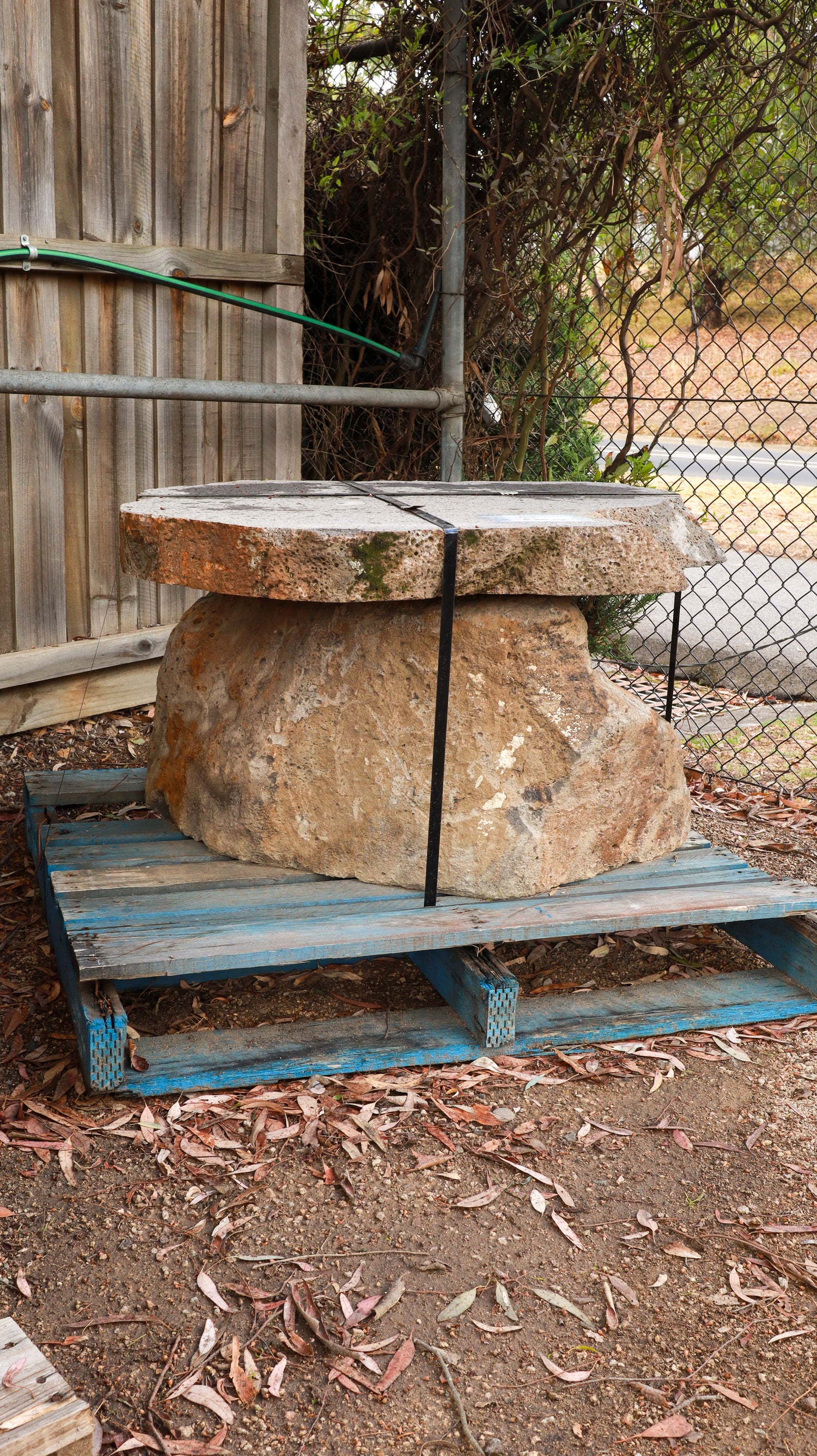 Large stone bench on a wooden pallet outdoors with a wooden fence and trees in the background.
