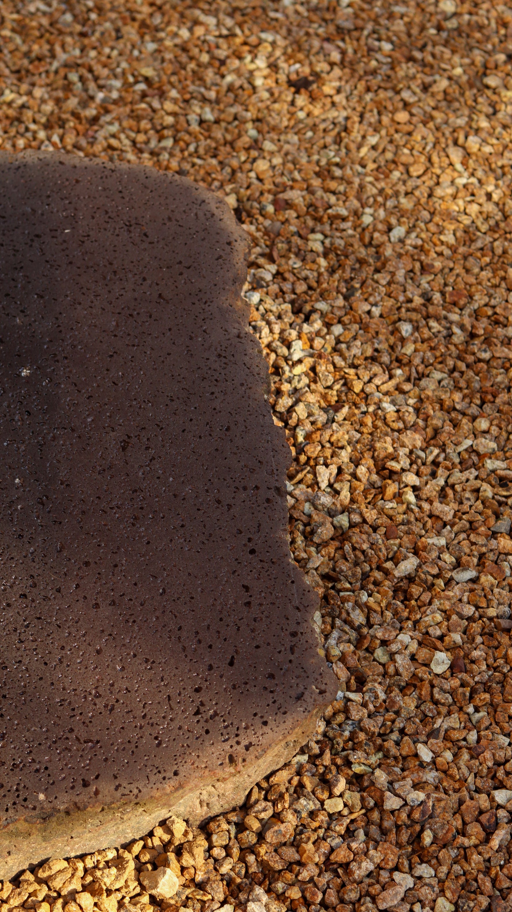 Close up of a large brown stone set in amongst smaller orangey-tan pebbles
