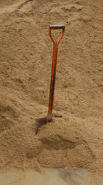An orange shovel in a large pile of sand