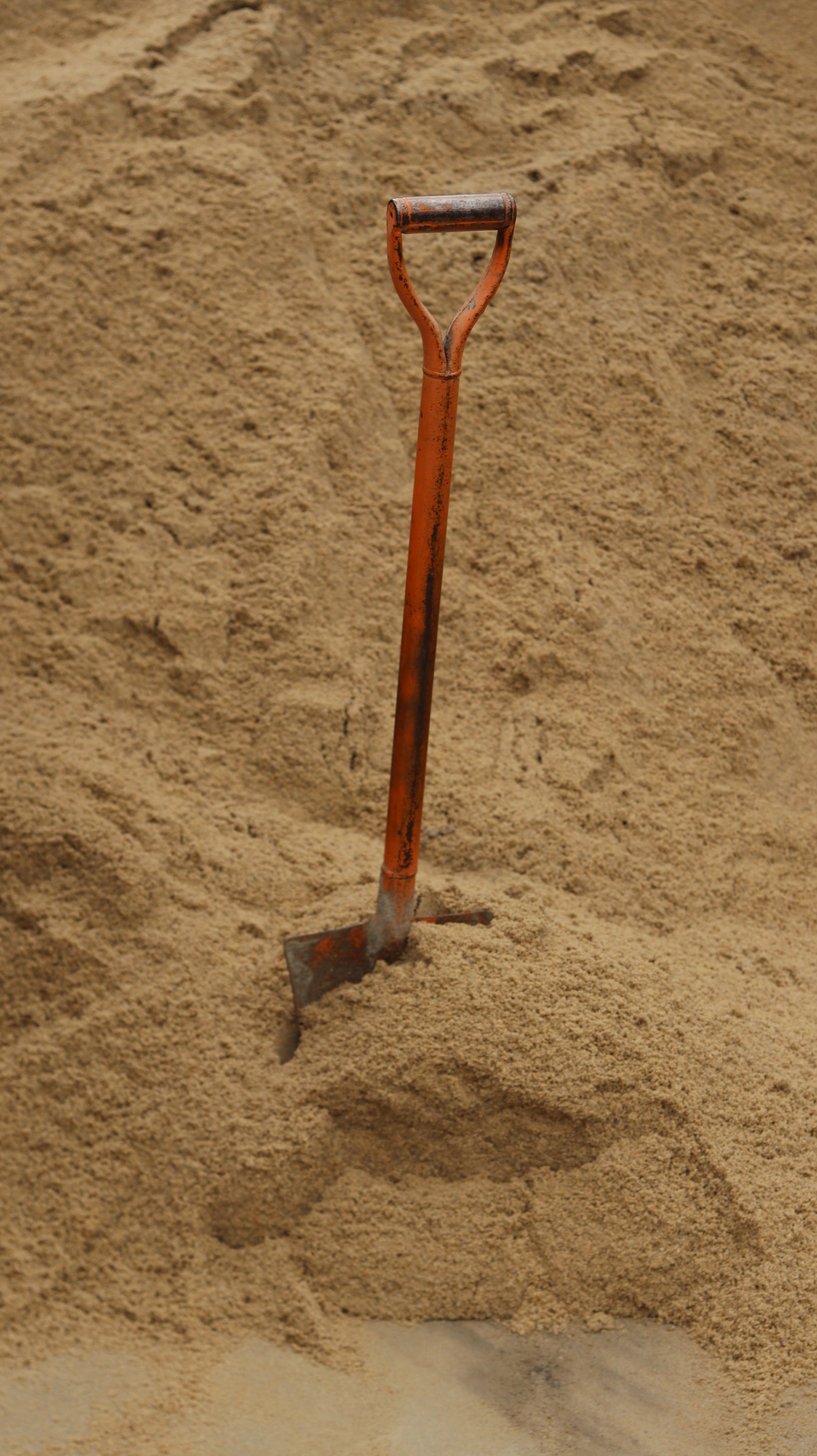 An orange shovel in a large pile of sand