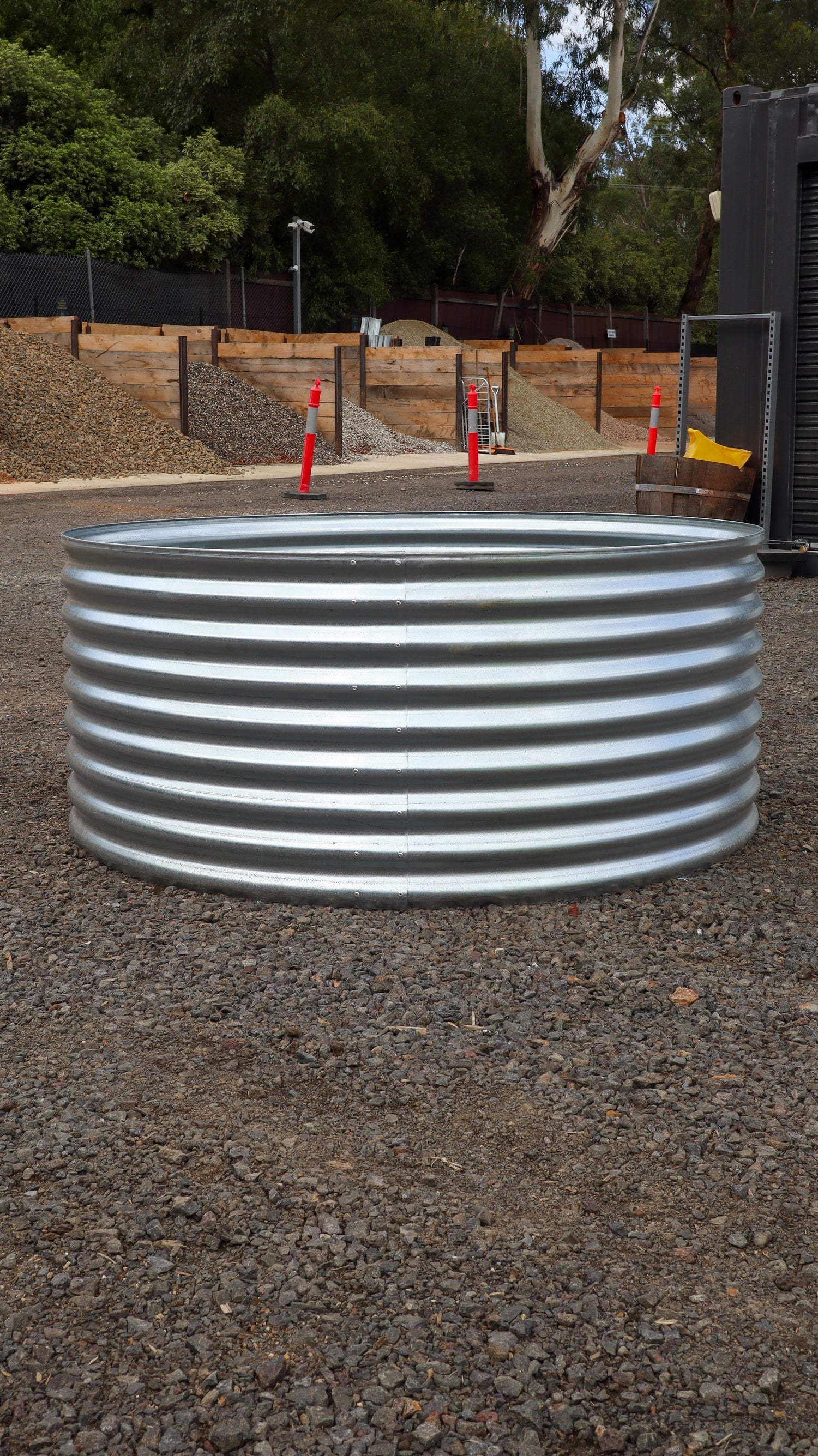 Metal water tank on a gravel surface with trees and a fence in the background