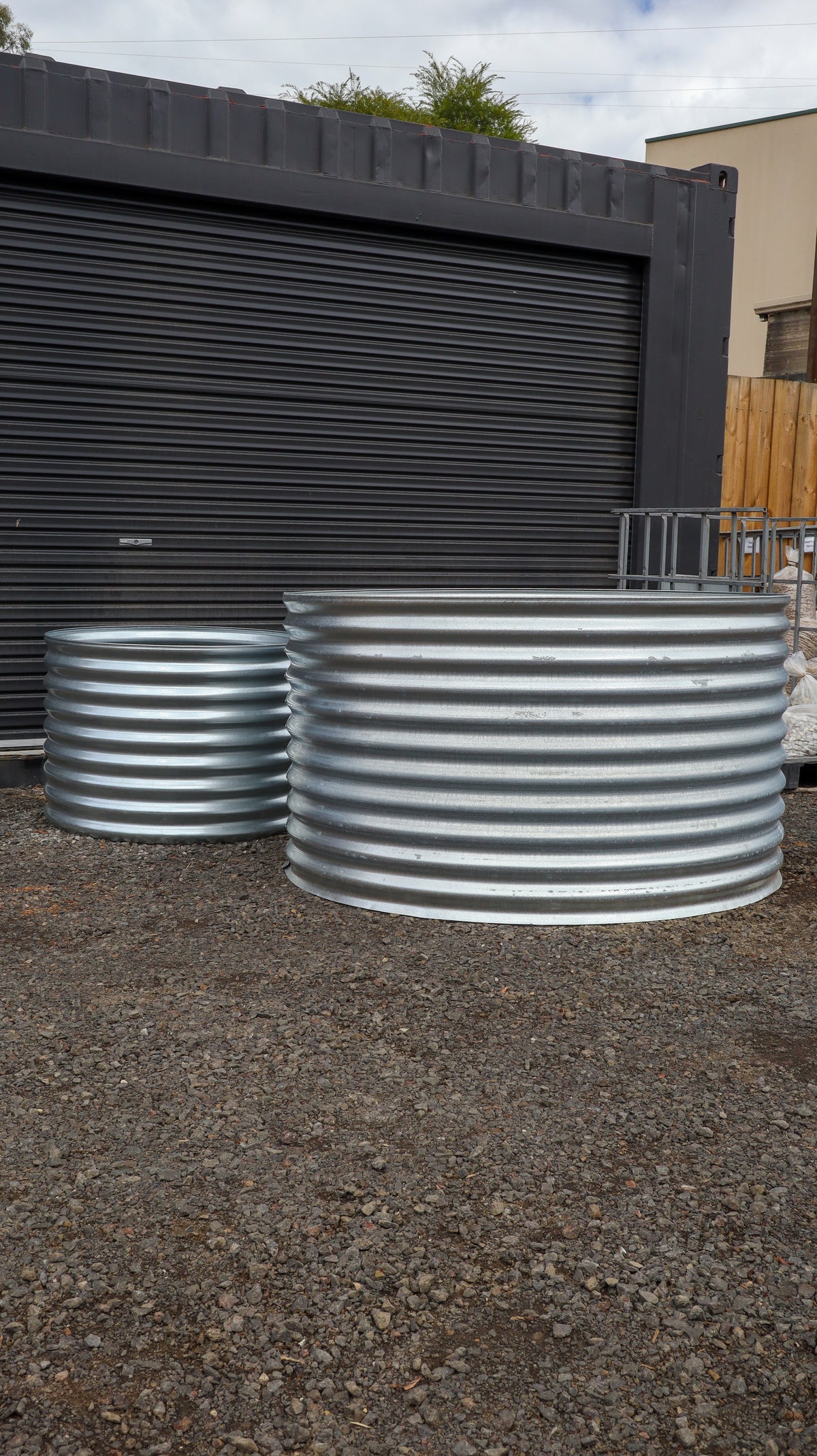 Two large metal water tanks on a gravel surface with a storage unit in the background.