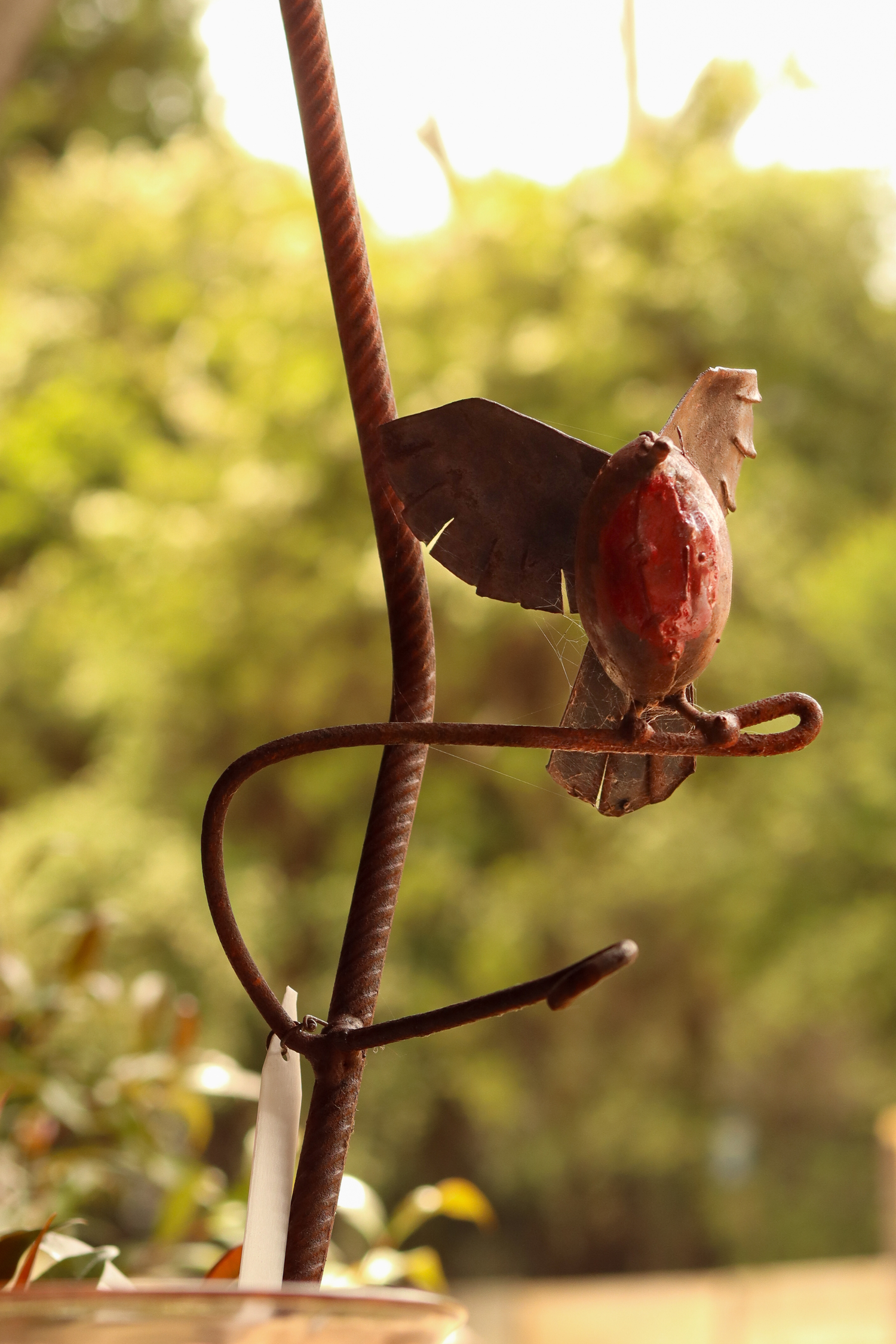 Metal sculpture of a bird on a branch with a blurred green background