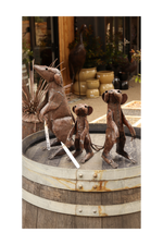 Three metal meerkat sculptures on a rustic wooden barrel with decorative elements in the background.