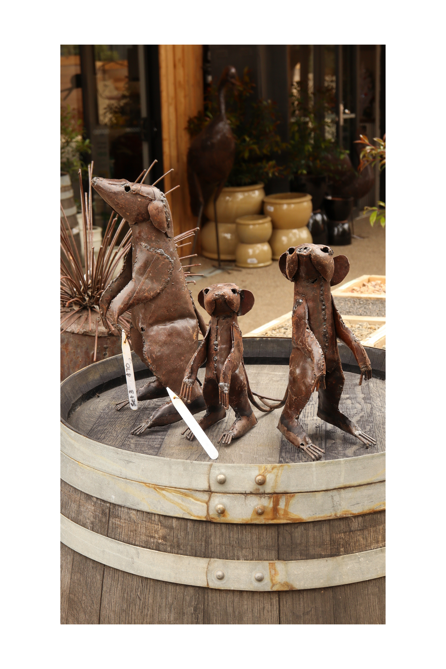 Three metal meerkat sculptures on a rustic wooden barrel with decorative elements in the background.