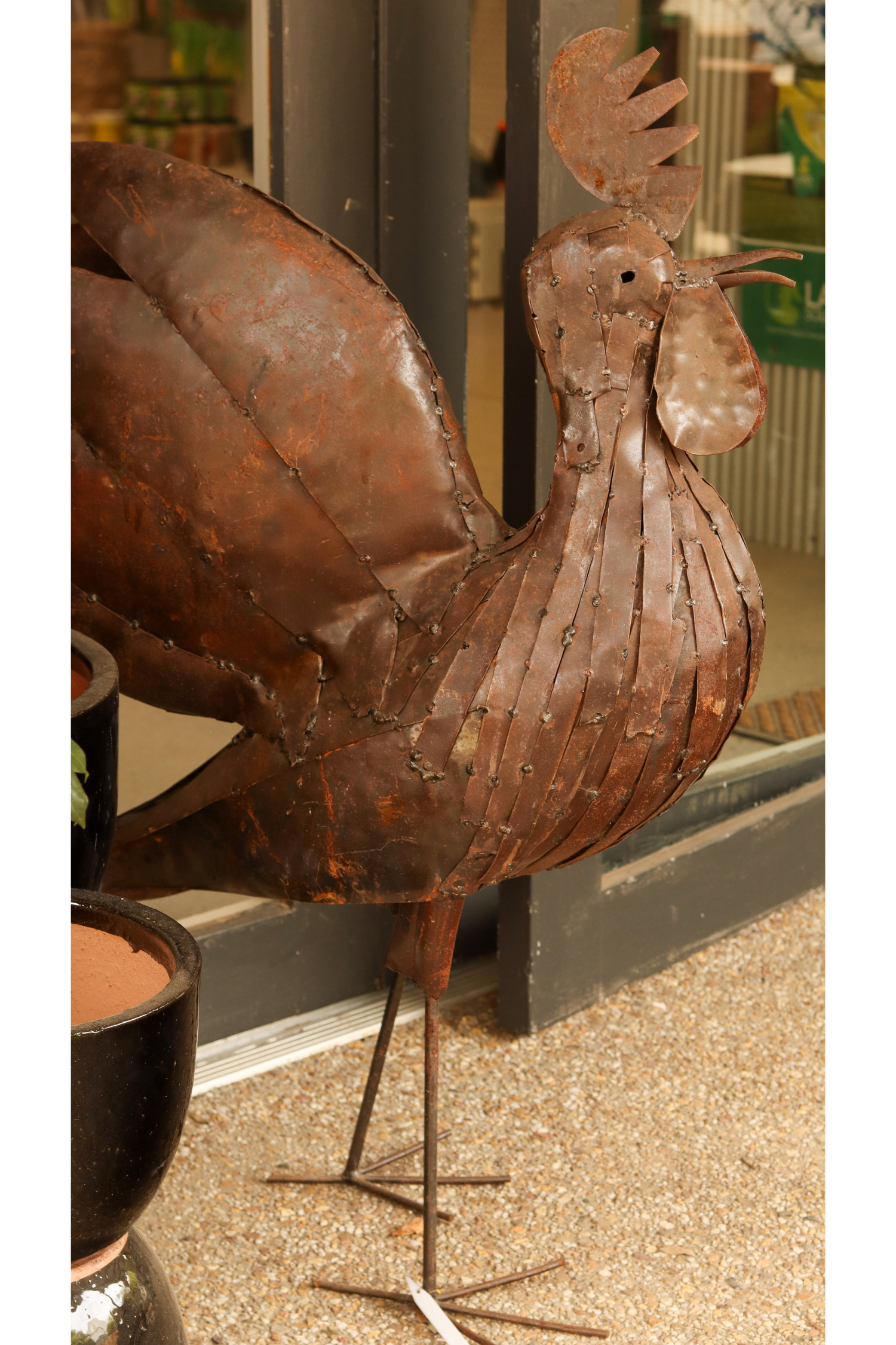 Rust-colored metal rooster sculpture on a stand