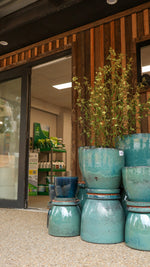 Stack of teal ceramic pots with plants inside, in front of a store entrance.
