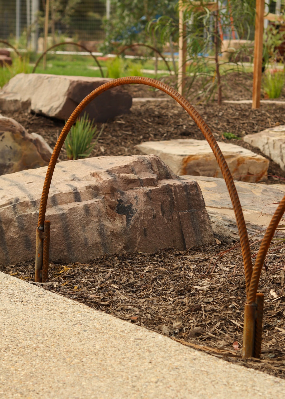 Rustic metal hoop in a garden setting with rocks and plants.