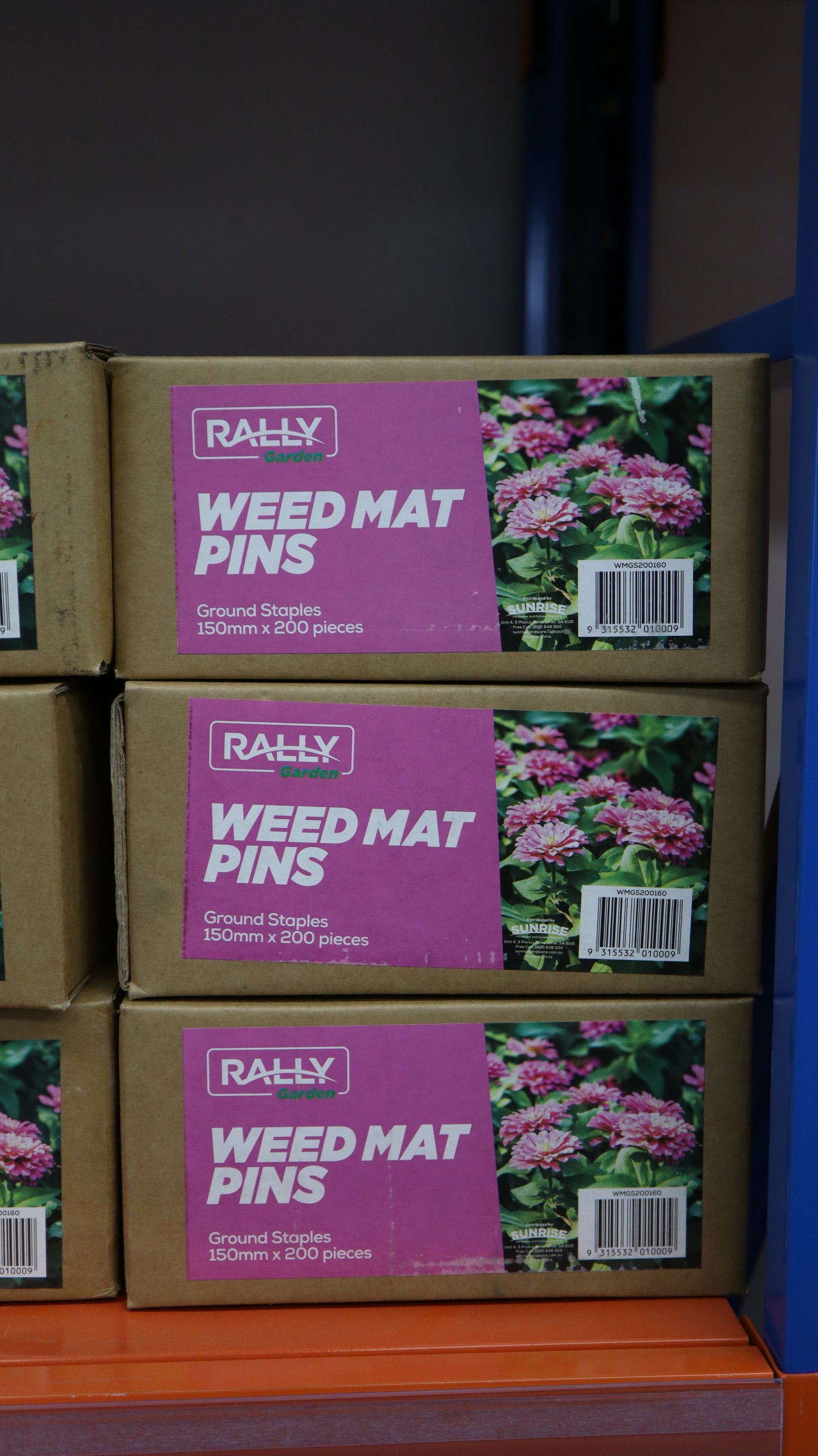 A stack of 3 boxes of weed mat pins with a pink label